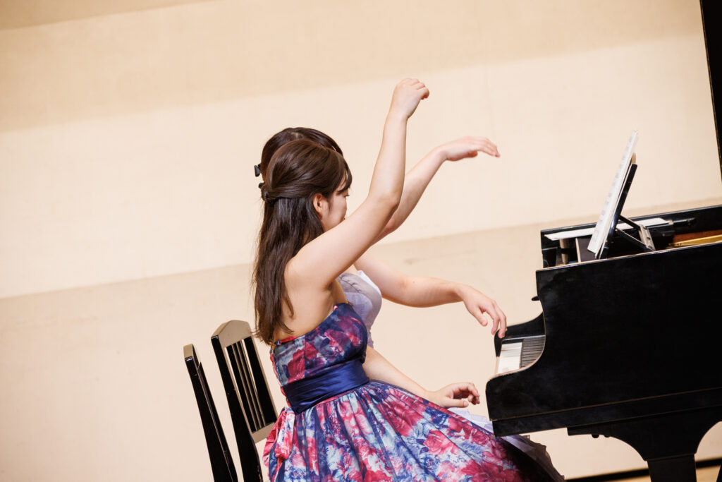 花柄のドレスを着て手をあげる女性とグランドピアノ